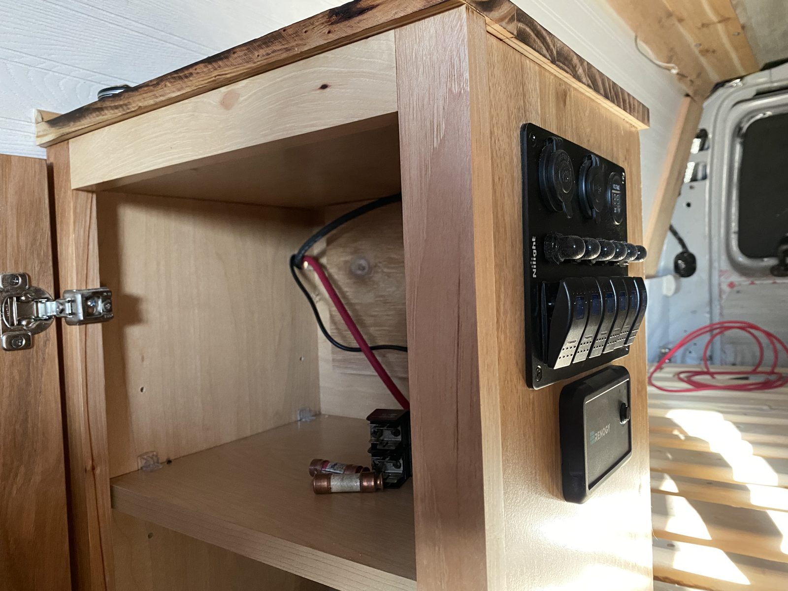 The switch panel built into the cabinet face inside the van, with rocker switches, twelve volt outlets, a voltmeter and the charge controller display